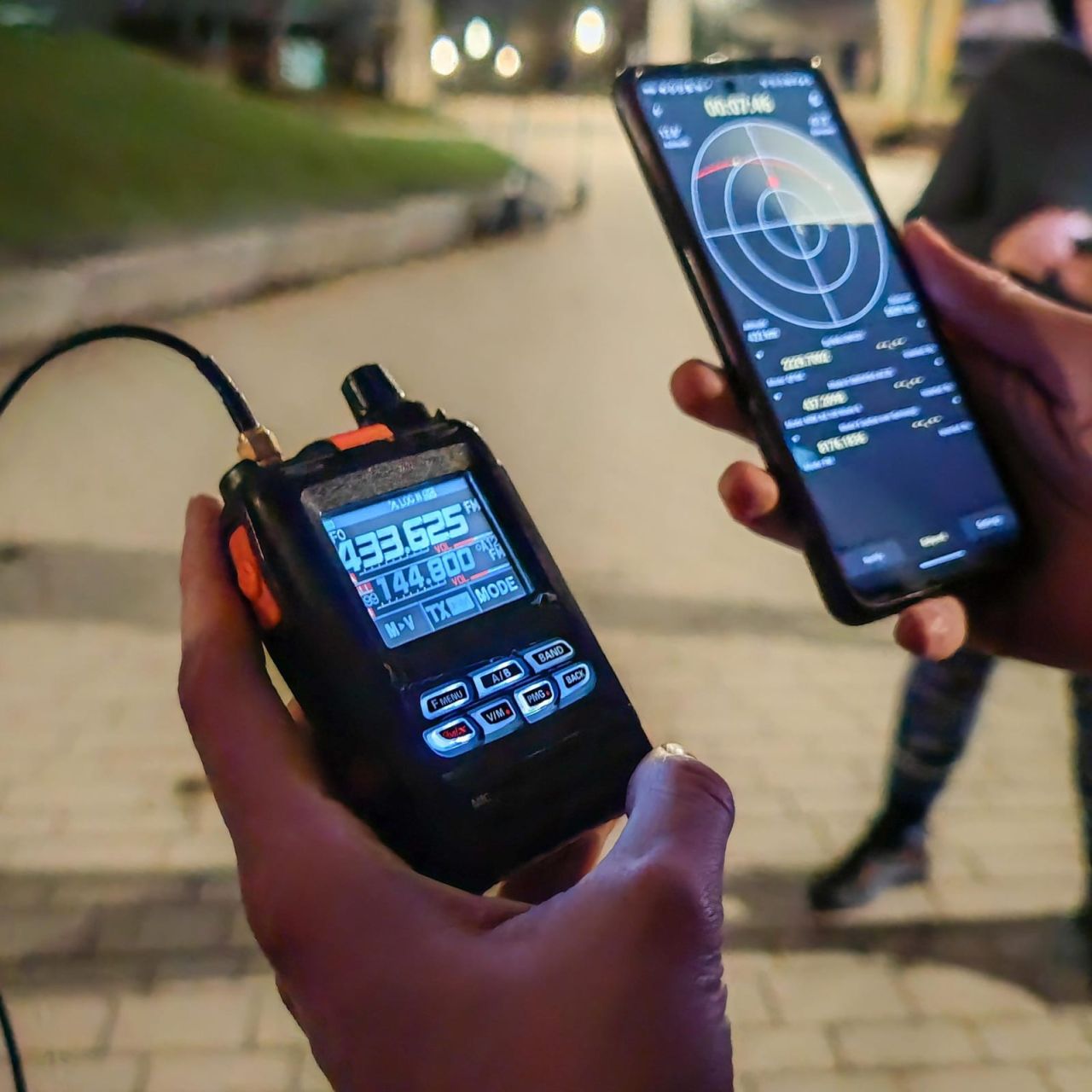 A handheld radio tuned to 433.625 MHz and a phone with a satellite tracking app